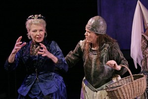 two women stood next to each other one with her hands out in front of her as though she is explaining something, the other woman who is wearing a knights armour is holding a wicker basket in one hand and has the other placed on the other woman's back