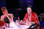 a woman in a traditional Chinese costume is sat next to a woman wearing a modern evening gown are at the dinner table eating and drinking