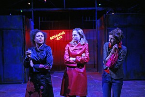 three woman are stood in a vertical line two are looking at one who is speaking, in the background there is a sign saying 'brennan's bar'